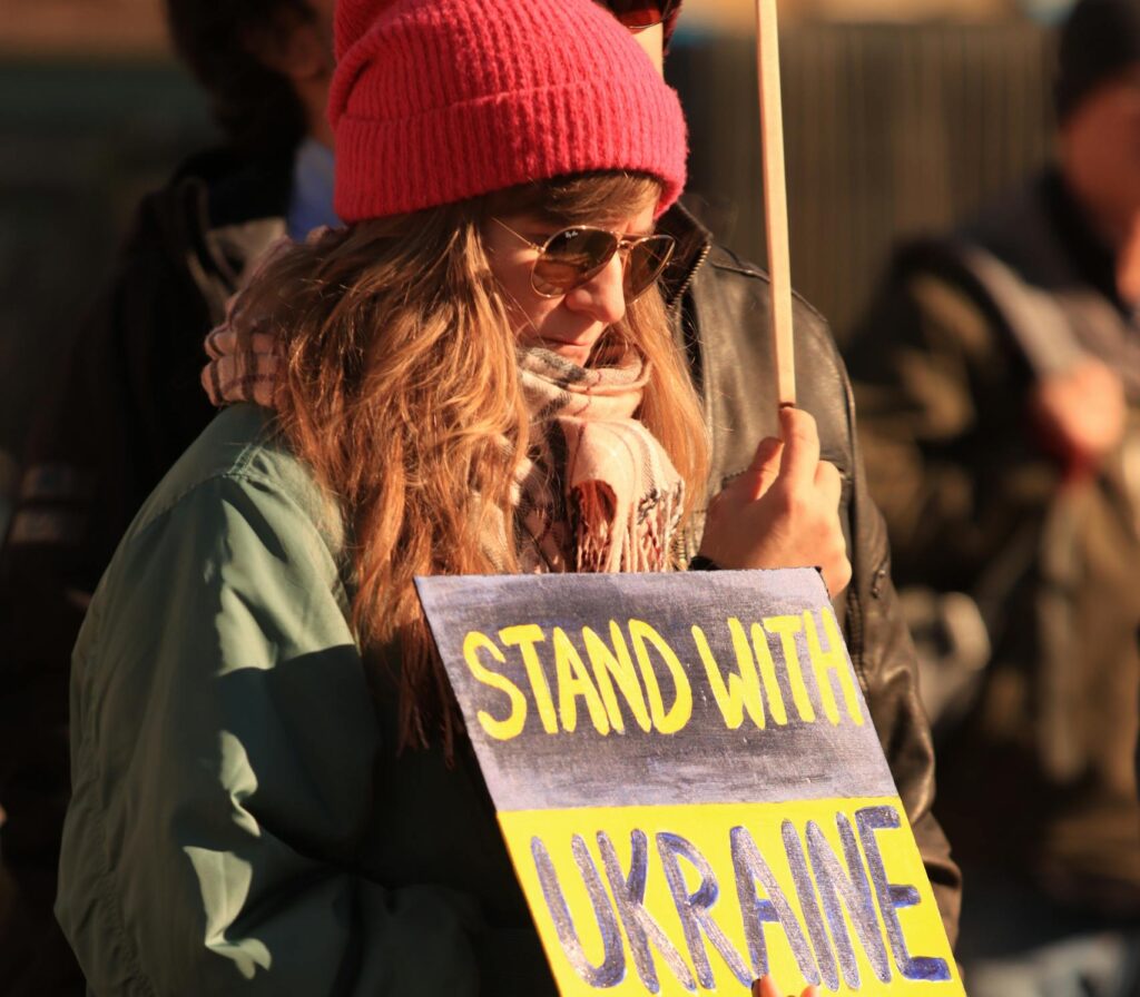 A person at an outdoor protest holds a 'Stand with Ukraine' sign in Gothenburg, Sweden.